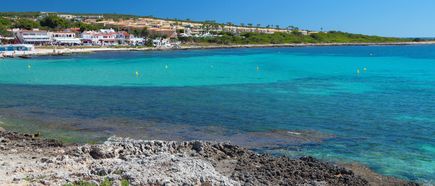 Küstenabschnitt Punta Prima auf Menorca mit türkisfarbenem Meer, flachem Strand und Blick auf die vorgelagerte Insel