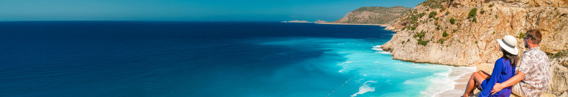 Paar blickt vom Aussichtspunkt auf das leuchtend blaue Meer und die steilen Felsen