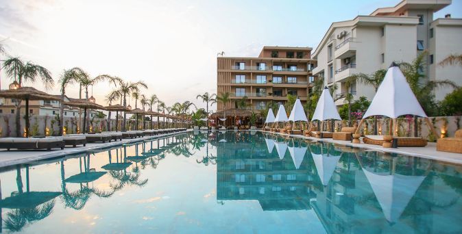 Großer Außenpool des Regina Palm Hotels mit Palmengarten, Bali-Betten, Sonnenschirmen und modernen Hotelgebäuden in einer gepflegten Resortanlage