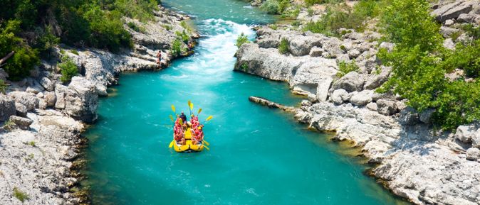 Gruppe beim Rafting auf türkisfarbenem Fluss, umgeben von Felsen und grüner Natur