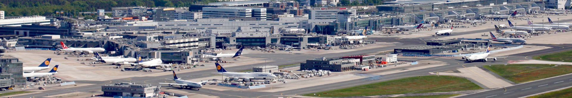 Luftaufnahme des Flughafens Frankfurt mit Terminalanlagen, Vorfeld, rollenden und abgestellten Flugzeugen verschiedener Airlines sowie Start- und Landebahnen im Hintergrund