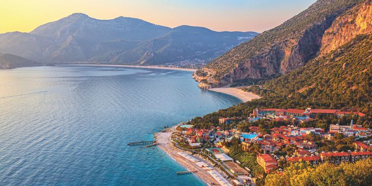 Panoramablick auf Ölüdeniz in der Türkei bei Sonnenuntergang mit ruhigem Meer, Sandstrand, grünen Bergen und Küstenort