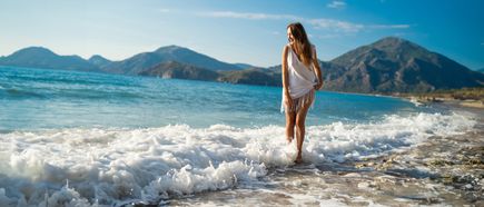 Frau steht lachend am Meer, während die Wellen sanft über den Strand rollen