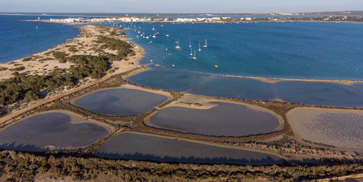 Blick auf die Lagune Estany des Peix auf Formentera mit klarem Wasser, kleinen Booten und umliegender Küstenlandschaft