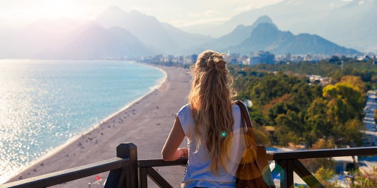 Person steht auf einer Terrasse mit weitem Blick über die Küste von Antalya in der Türkei, türkisblaues Meer und grüne Landschaft im Hintergrund