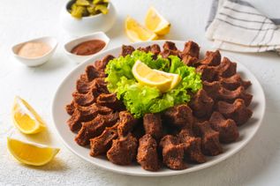 Çiğ Köfte in kleinen Portionen auf Teller, mit grünem Salat und Zitronenspalten serviert