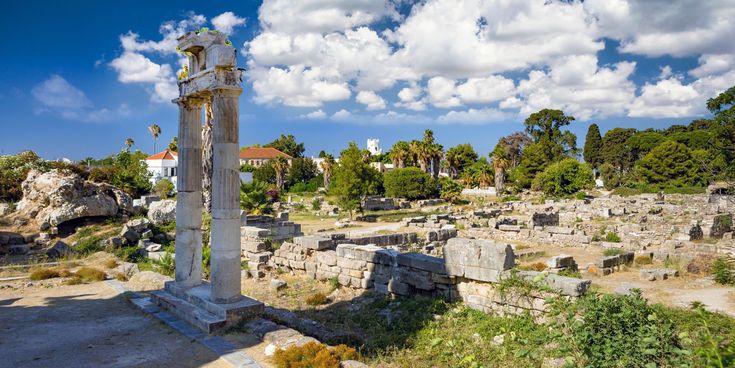 Antike Ruinen mit zwei hohen Säulenresten und verstreuten Steinmauern unter blauem Himmel mit Wolken
