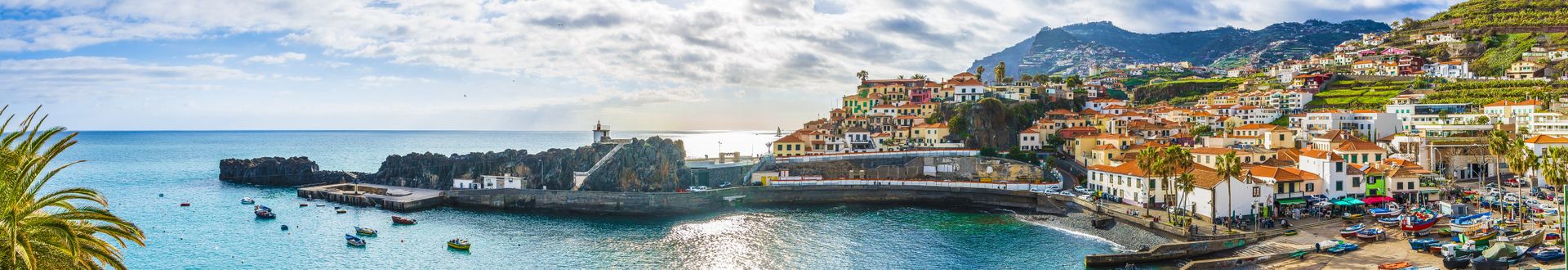 Panoramablick auf den Hafen von Câmara de Lobos auf Madeira mit Fischerbooten, Wellenbrechern, bunten Häusern an den Berghängen und dem Atlantik