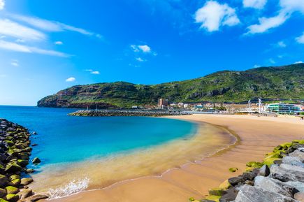 Sandstrand Praia de Machico auf Madeira mit geschützter Badebucht, türkisblauem Wasser, Wellenbrechern und grünen Berghängen