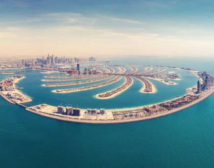 Luftaufnahme von Dubai mit künstlichen Inseln in Form von Palmen und einer Skyline mit Wolkenkratzern im Hintergrund