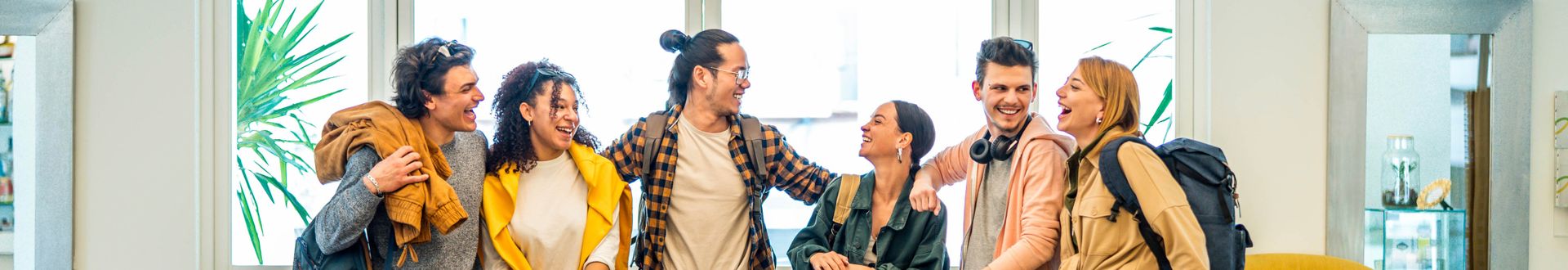 „Gruppe junger Reisender steht lächelnd und miteinander sprechend im Eingangsbereich eines Hotels