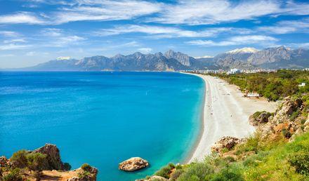 Panoramablick auf den Konyaalti-Strand in der Türkei mit türkisblauem Meer, hellem Kiesstrand und Bergkulisse im Hintergrund