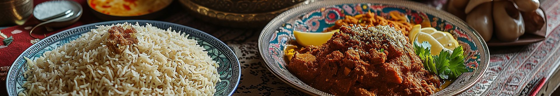 Orientalisches Menü mit Reis auf dekorativem Teller und würzigem Fleischragout in Schale, dazu Zitrone und Kräuter