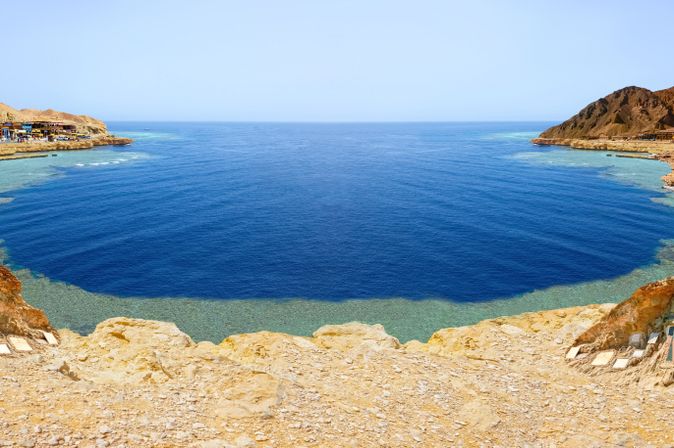Blick auf das berühmte Blue Hole bei Dahab in Ägypten mit tiefblauem Meer, hellen Küstenfelsen und umliegenden Bergen