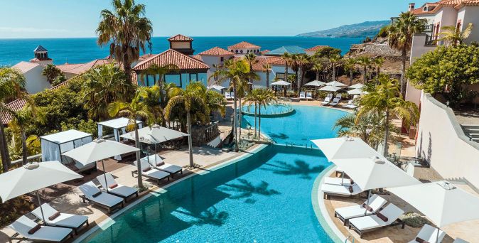 Luxuriöses Hotelresort auf Madeira mit mehreren Pools, Palmen, Liegen und Sonnenschirmen in einer terrassenförmigen Anlage mit Blick auf das Meer