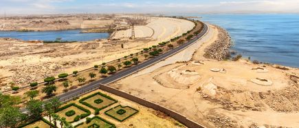 Luftaufnahme des Assuan-Hochdamms mit angrenzendem Nil, Wüstenlandschaft und symmetrischem Gartenmuster im Vordergrund