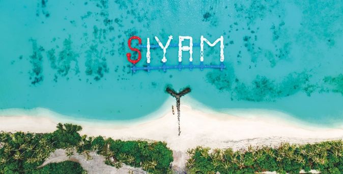Luftaufnahme eines weißen Sandstrands mit türkisfarbenem Wasser und dem Schriftzug 'SIYAM'