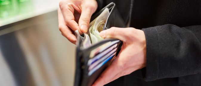 Hände öffnen eine schwarze Geldbörse mit mehreren Kartenfächern und sichtbaren Geldscheinen.