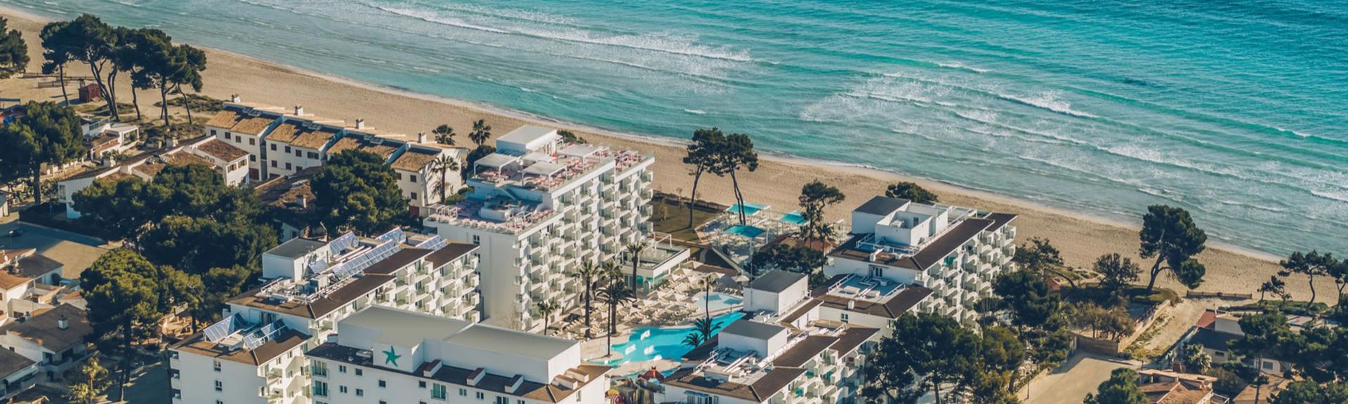 Luftaufnahme eines Hotels mit mehreren Gebäuden, Pool und Strand im Hintergrund