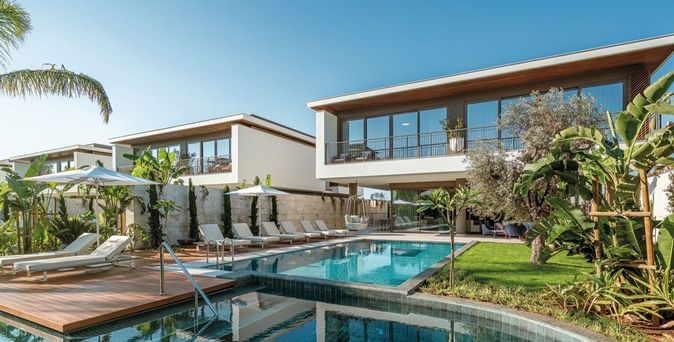 Moderner Hotelpool mit Liegestühlen und Sonnenschirmen, umgeben von tropischen Pflanzen und zweistöckigem Gebäude