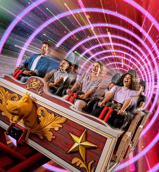 Fahrgäste in einer Holzachterbahn mit goldfarbenen Sternen und Verzierungen vor einem Hintergrund aus pinken und grünen Lichtkreisen im Dubai Motiongate.