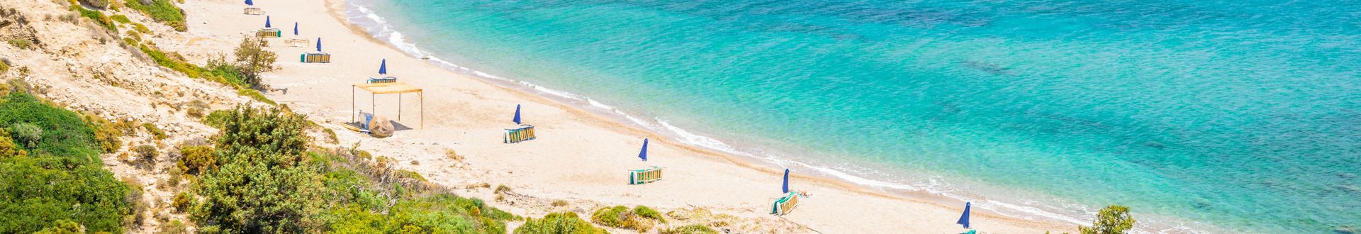 Strand mit Kieselsteinen und Wellen am Ufer vor einer Berglandschaft unter blauem Himmel an der Küste von Kos