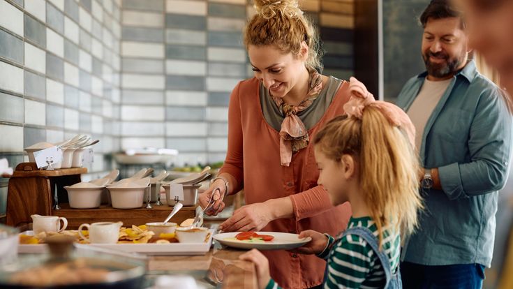 Familie bedient sich gemeinsam an einem Buffet mit verschiedenen Speisen