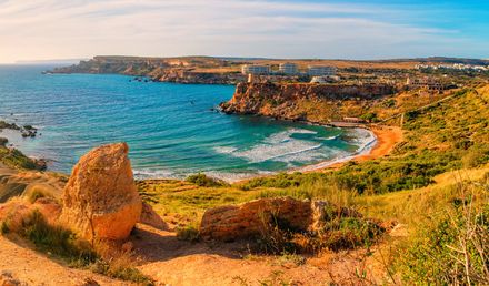 Ghajn Tuffieha Bay auf Malta mit Blick auf die felsige Küstenlandschaft, die geschwungene Sandbucht und das türkisfarbene Mittelmeer unter blauem Himmel
