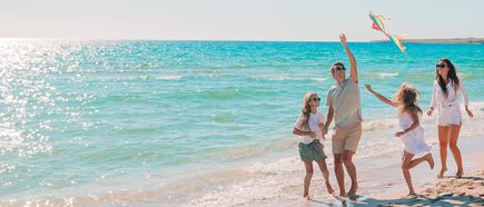 Familie mit zwei Kindern spielt und lässt einen Drachen am Strand im Sonnenschein steigen
