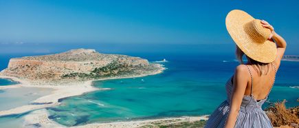Person mit Sonnenhut blickt auf die Balos-Lagune auf Kreta in Griechenland mit türkisblauem Meer, heller Sandbank und felsiger Insel im Hintergrund