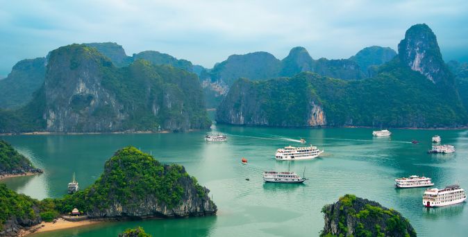 Blick auf eine Bucht in Vietnam mit mehreren Booten auf grünem Wasser und bewaldeten Kalksteininseln