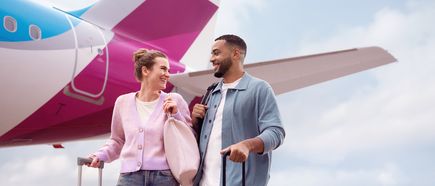 Zwei Reisende mit Rollkoffern stehen vor dem Heck eines Eurowings Airbus A320neo