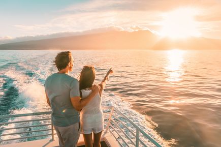 Zwei Personen stehen auf dem Deck eines Schiffes und blicken bei Sonnenuntergang über das Meer