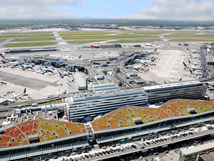 Luftaufnahme des Flughafens Frankfurt mit Terminalgebäuden, Vorfeld, mehreren Lufthansa-Flugzeugen, Start- und Landebahnen sowie dem sichtbaren Schriftzug „Frankfurt Airport“ auf dem Terminaldach