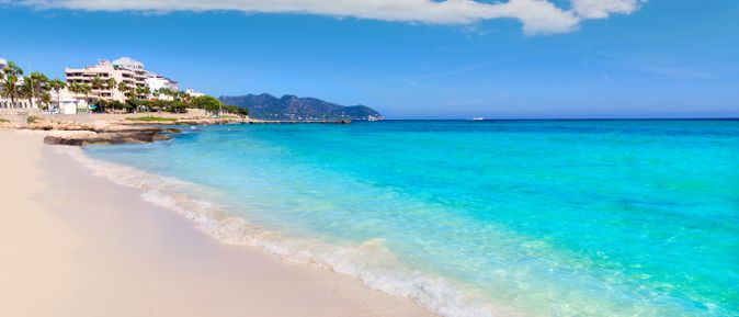 Strand von Cala Millor mit hellem Sand, türkisblauem Wasser und Promenade mit Hotels und Palmen