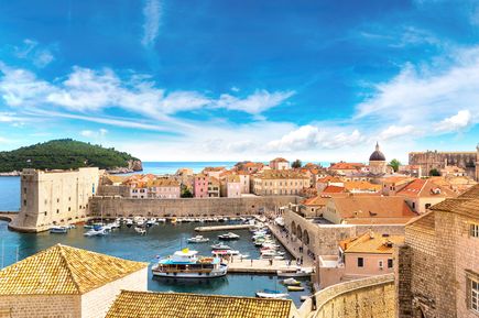 Panoramablick auf die historische Altstadt von Dubrovnik in Kroatien mit Stadtmauer, Hafenbecken, Booten, Terrakottadächern und der Adria im Hintergrund
