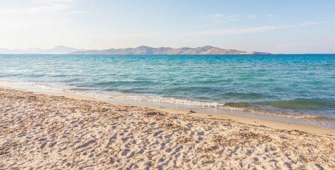 Sandstrand mit sanften Wellen und einer Insel am Horizont unter klarem Himmel