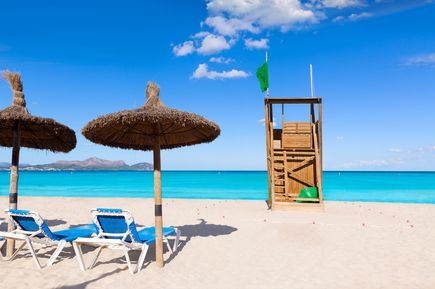 Strand von Can Picafort mit Liegen, Sonnenschirmen und hölzernem Rettungsturm vor türkisblauem Meer