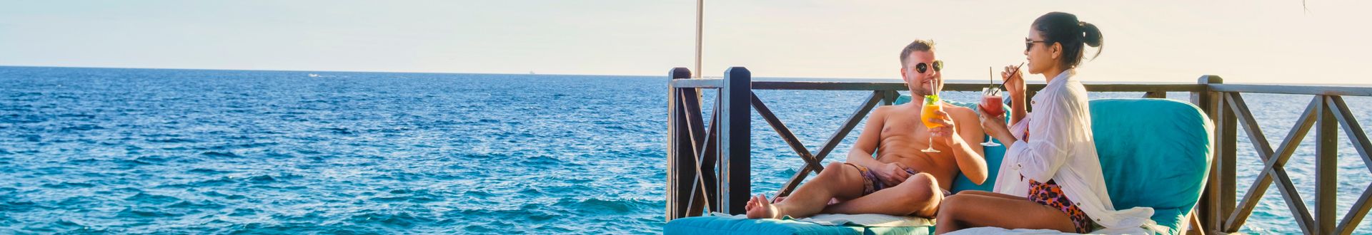Zwei Personen sitzen entspannt auf einer Terrasse am Meer und trinken Cocktails