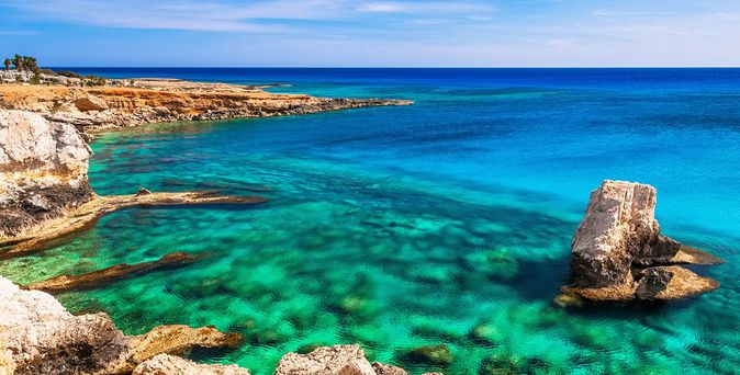 Klares türkisfarbenes Meer an felsiger Küste in Zypern unter blauem Himmel