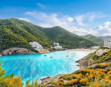 Bucht Cala Llonga auf Ibiza mit türkisblauem Wasser, grünen Hügeln und weißen Hotelanlagen am Strand