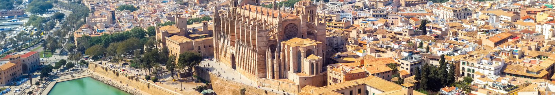 Luftaufnahme von Palma de Mallorca mit der Kathedrale La Seu im Vordergrund, dem angrenzenden Stadtsee mit Springbrunnen und Blick auf die Stadt und Berge im Hintergrund