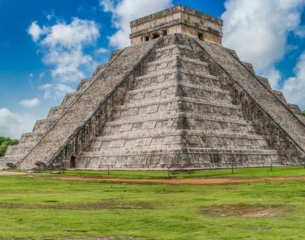 Große steinerne Pyramide mit breiten Stufen und flachem Tempelbau an der Spitze unter blauem Himmel