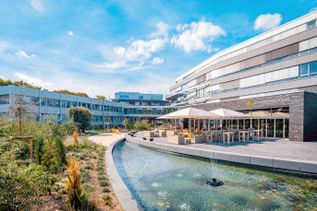 Außenansicht des Firmengebäudes von schauinsland-reisen mit moderner Glasfassade, begrüntem Innenhof, Wasserbecken mit Springbrunnen und Terrasse mit Sonnenschirmen