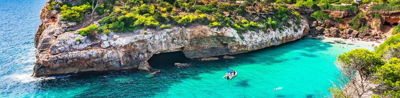 Kleine Bucht mit türkisfarbenem Wasser, umgeben von felsigen Klippen und grüner Vegetation, mit einem Boot auf dem Wasser.