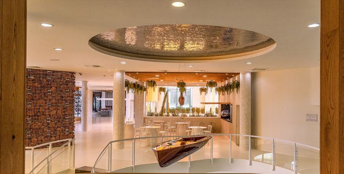 Heller, moderner Lounge- und Aufenthaltsbereich im Higueron Hotel Malaga, Curio Collection by Hilton, mit zentralem Sitzbereich, hängender Installation in der Mitte, Pflanzenarrangements und dekorativer Deckenstruktur.