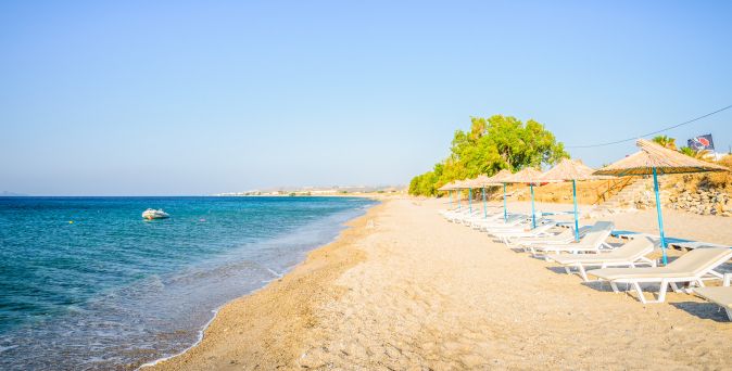 Strand mit Liegestühlen und Sonnenschirmen entlang des Wassers unter klarem Himmel