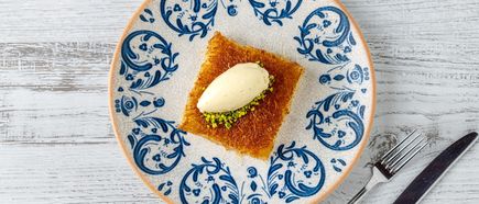 Stück Künefe auf gemustertem Teller, goldbraun gebackenes Fadendessert mit cremiger Füllung und Pistazien