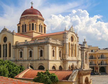 Große Kirche mit roter Kuppel und Glockenturm vor bewölktem Himmel, umgeben von Bäumen und Gebäuden.