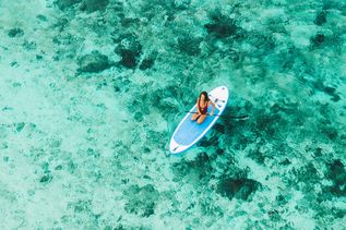 Eine Frau paddelt auf einem Stand-Up-Paddle-Board in klarem, türkisfarbenem Wasser mit sichtbarem Meeresboden.